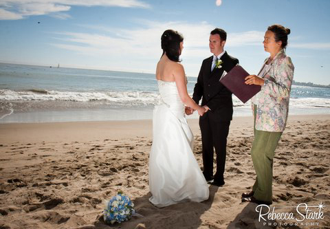 Corrina officiating a wedding on the beach, the couple facing each other at the water's edge