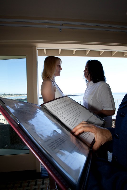 A couple exchanging vows indoors with the Santa Cruz coastline visible through the windows